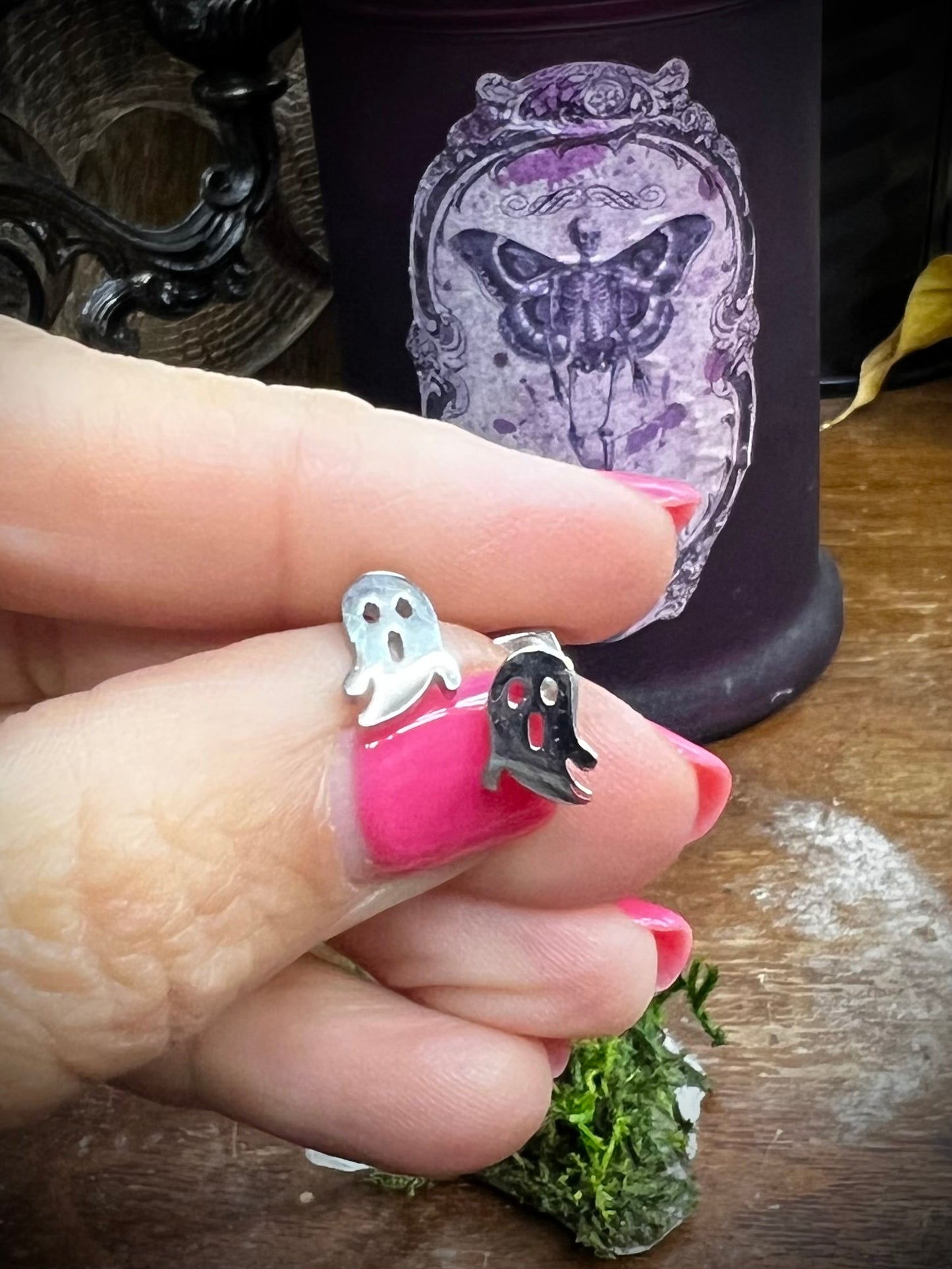 Hand holding two silver ghost-shaped rings with a decorative background