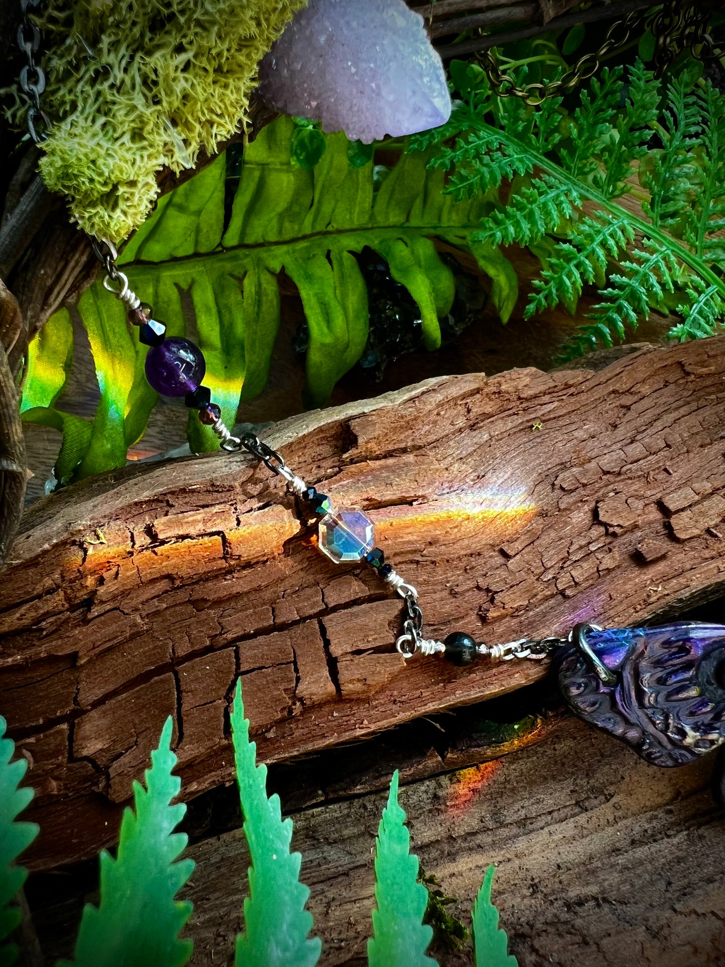 Amethyst and obsidian bead details of moth necklace held in hand with greenery background