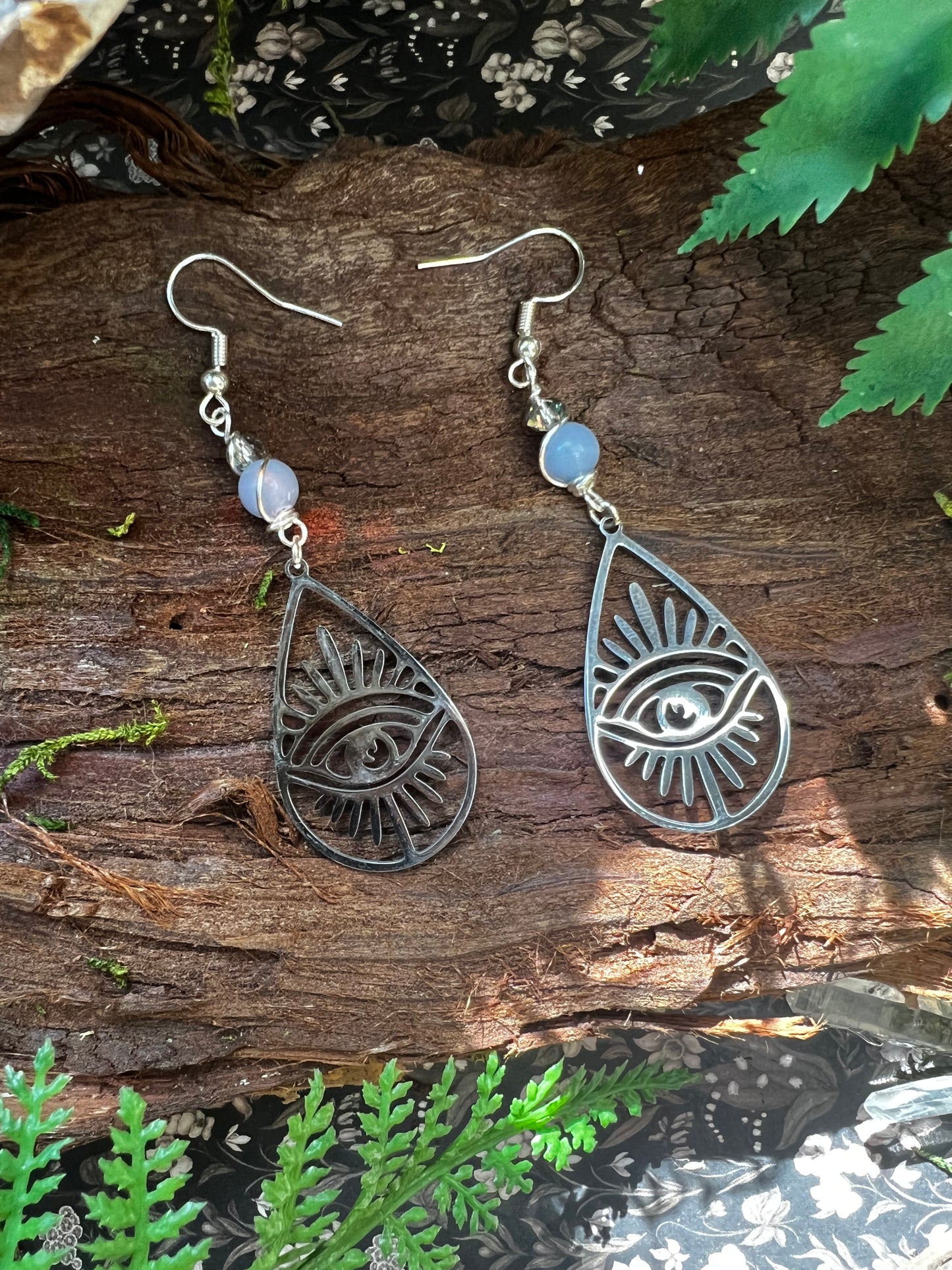 Angelite and iridescent eye earrings displayed on wood with forest elements