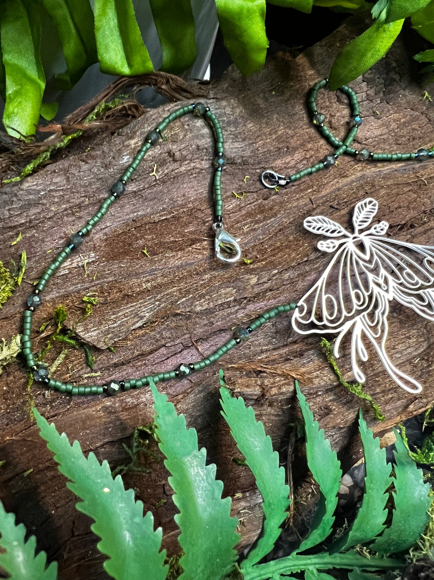Flat lay of luna moth necklace arranged on rustic wooden background with natural greenery accents