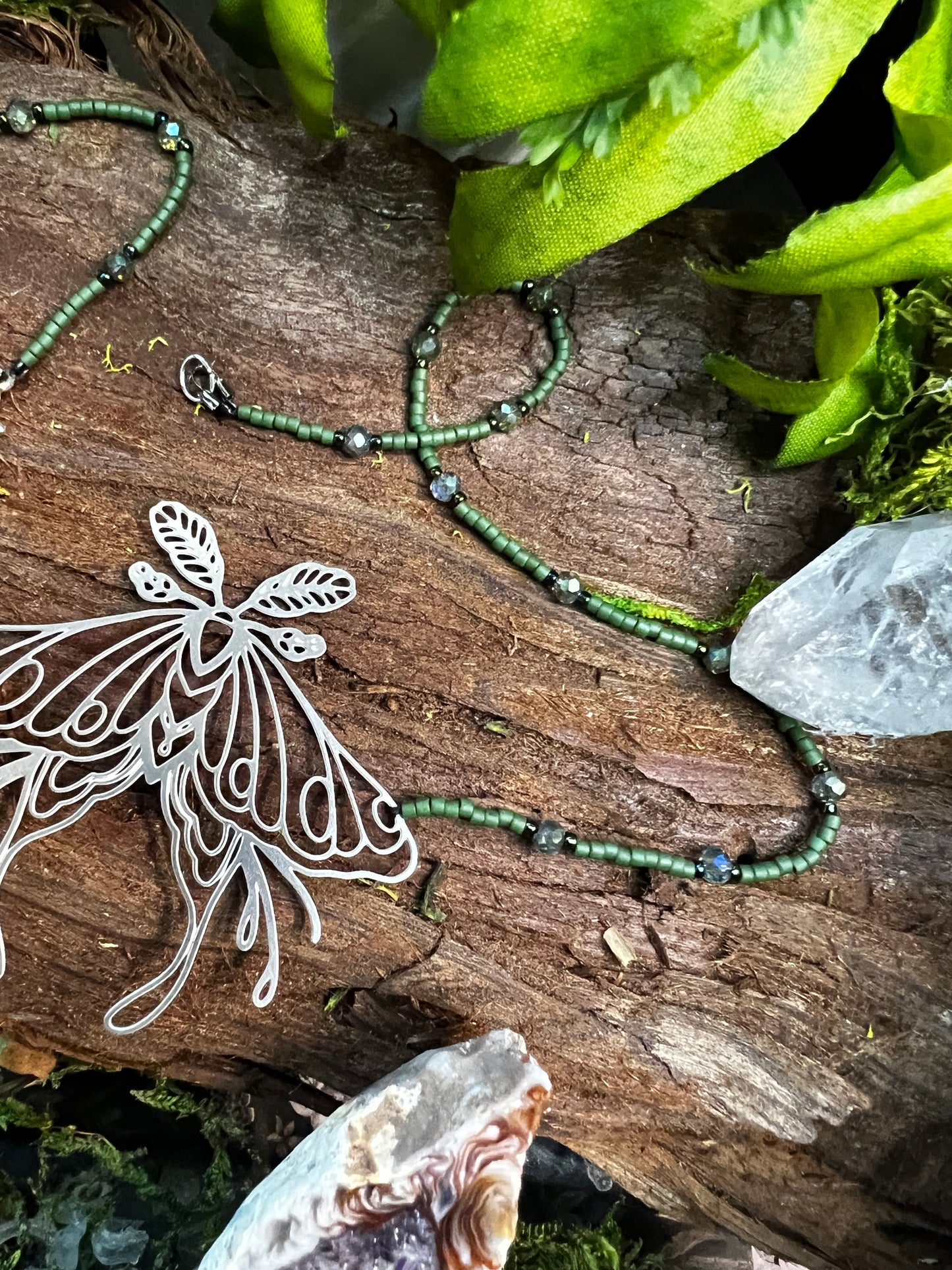 Necklace draped on a moss and fern backdrop with visible shimmer of forest-inspired beads