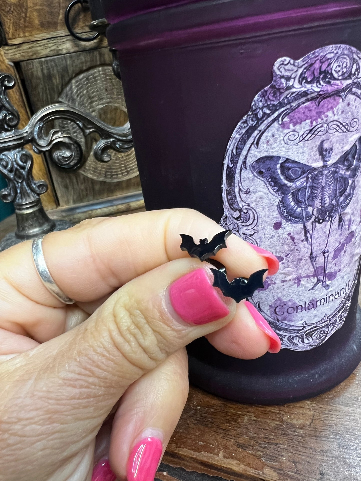Hand holding a black bat-shaped earring with a decorative book in the background