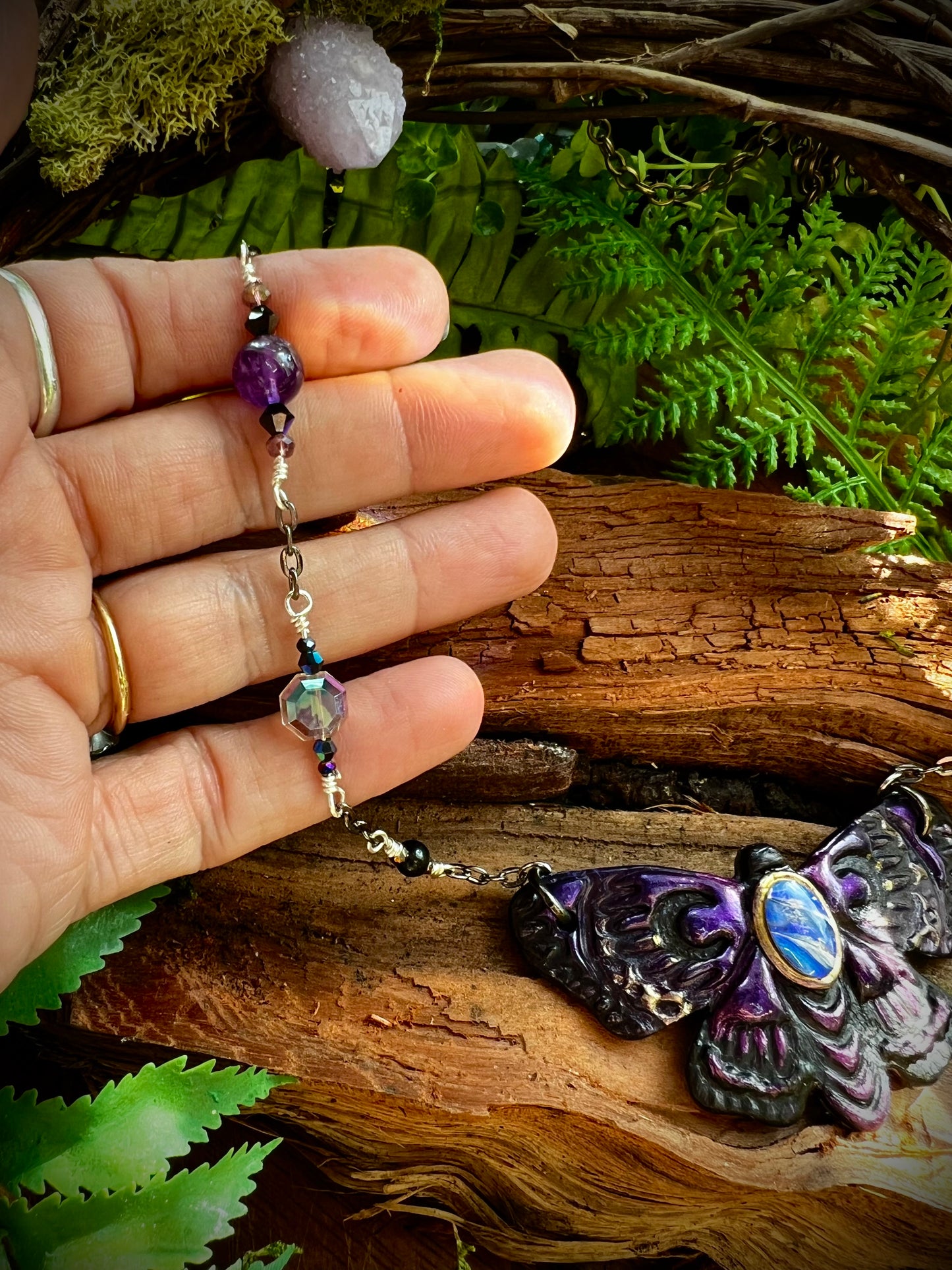 Unique artisan moth necklace with gemstone beads displayed among ferns and quartz