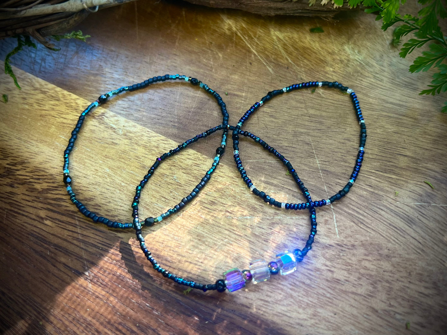 Three beaded bracelets on a wooden surface with a plant in the background