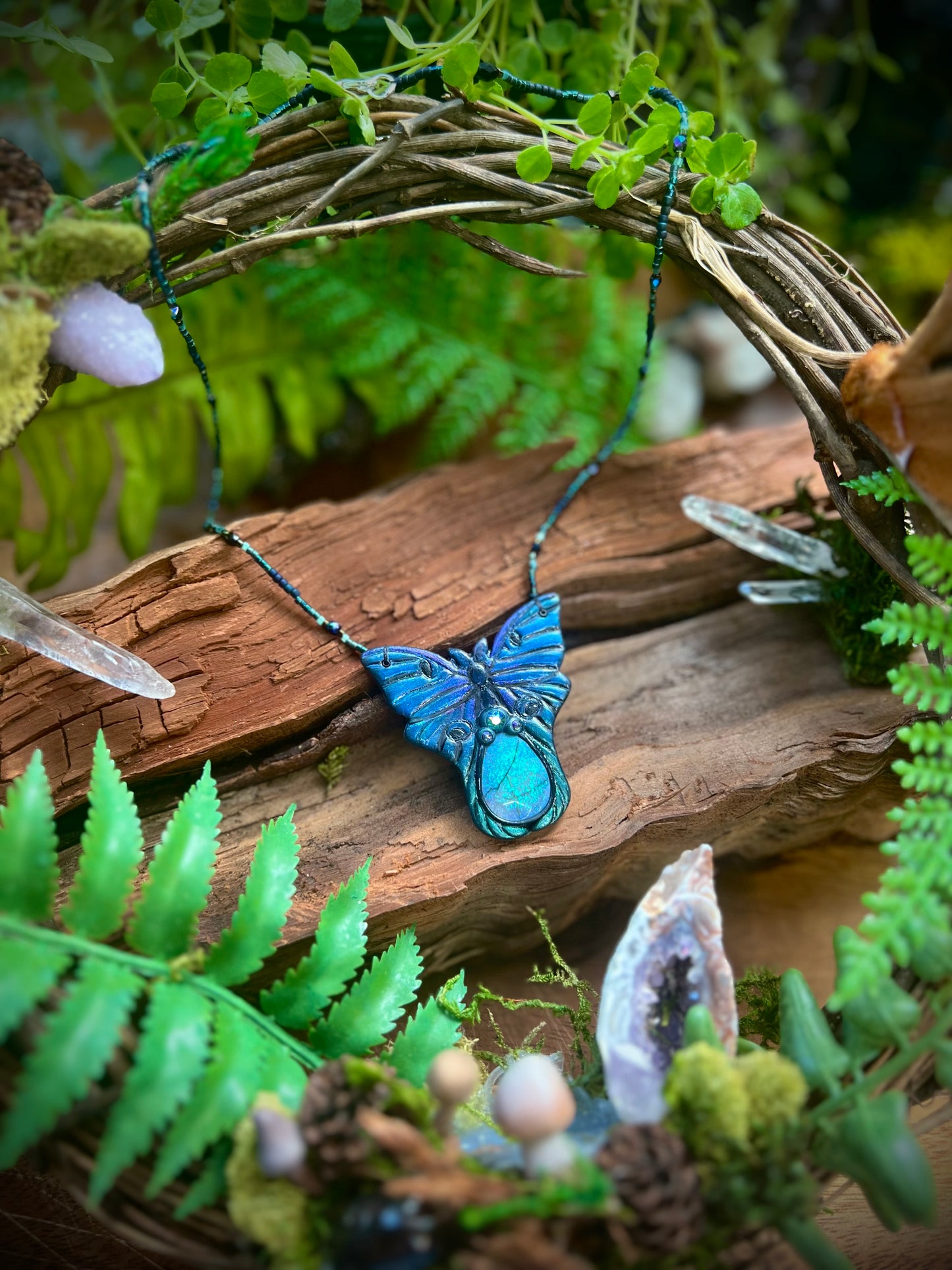 Artisan luna moth opal necklace displayed against rustic wood and ferns