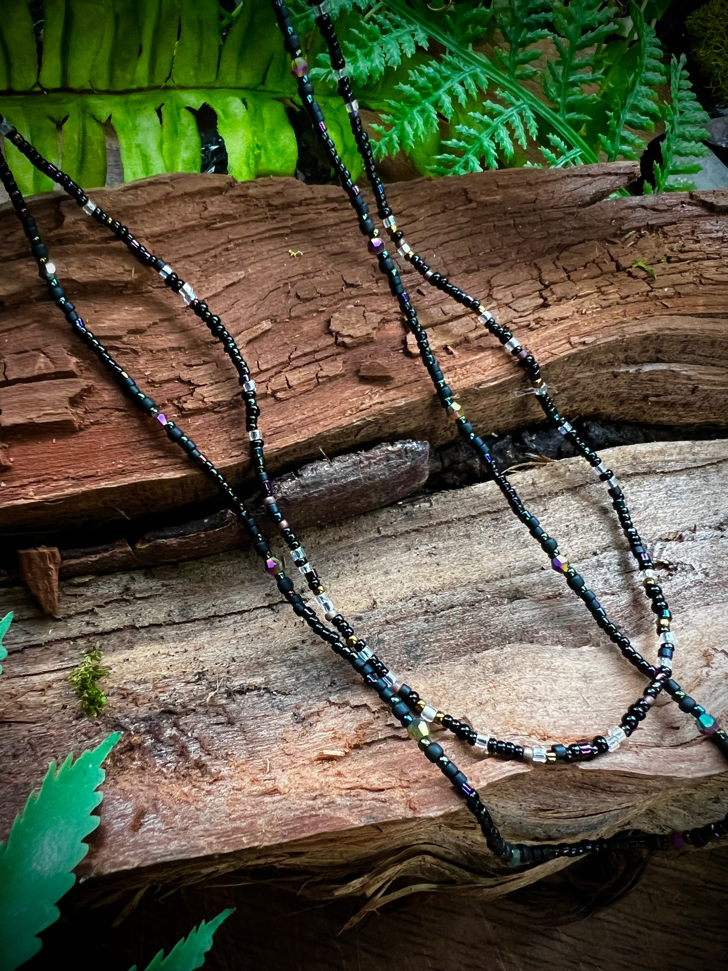 Necklace with beads on a wooden surface with ferns in the background