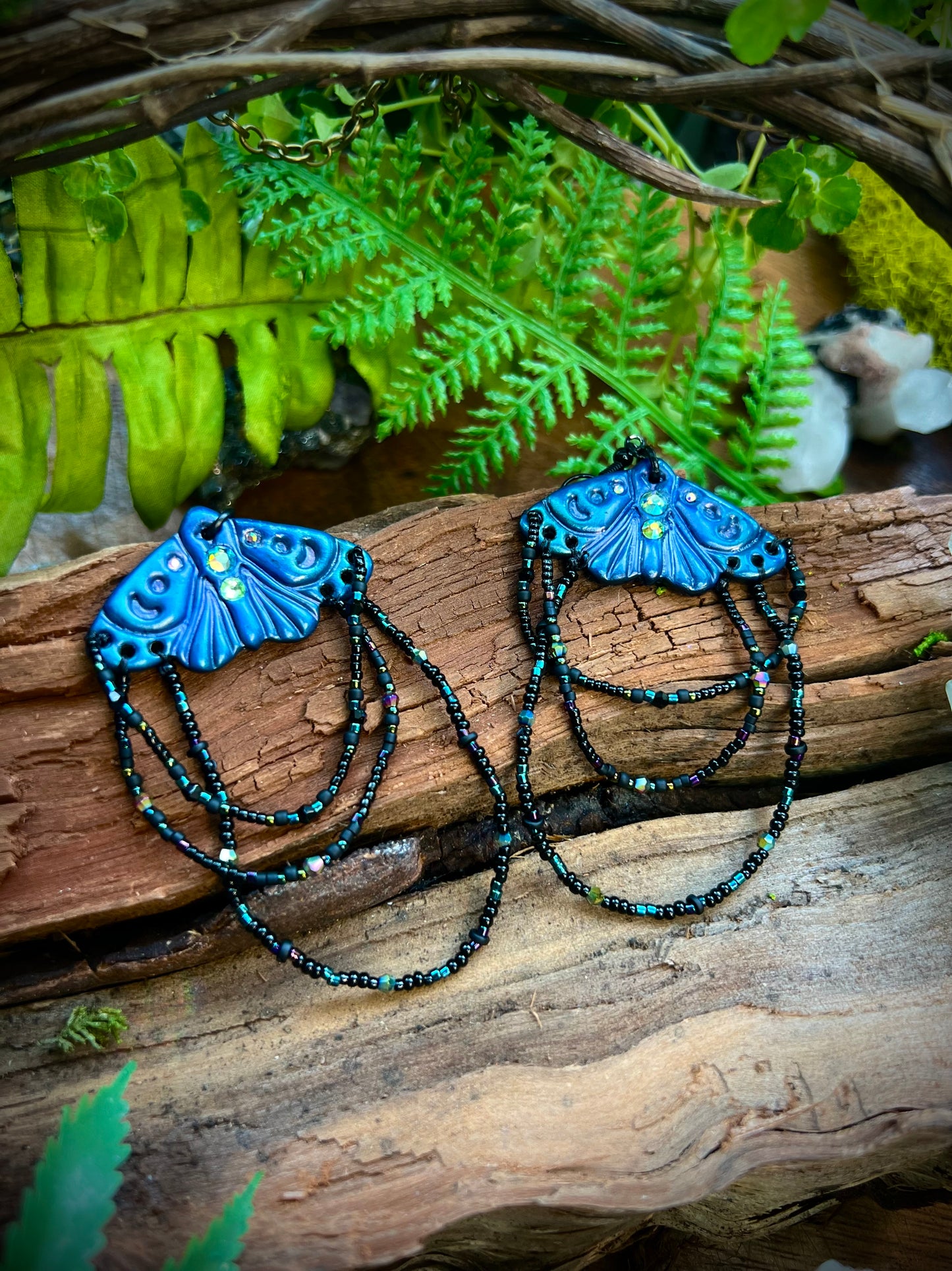Mystical moth earrings displayed against wood and greenery