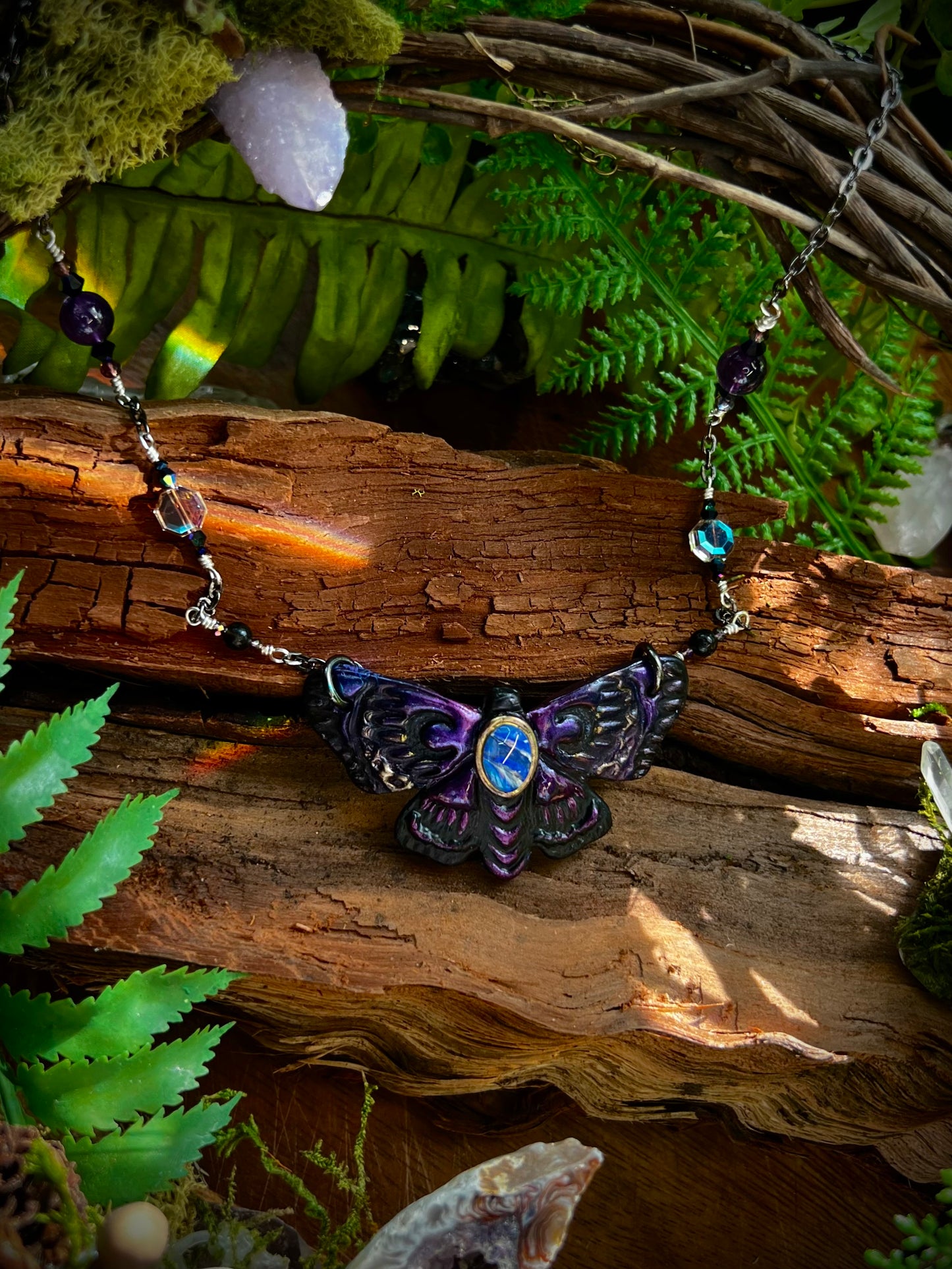 Mystical moth necklace with gemstone beads displayed against rustic wood