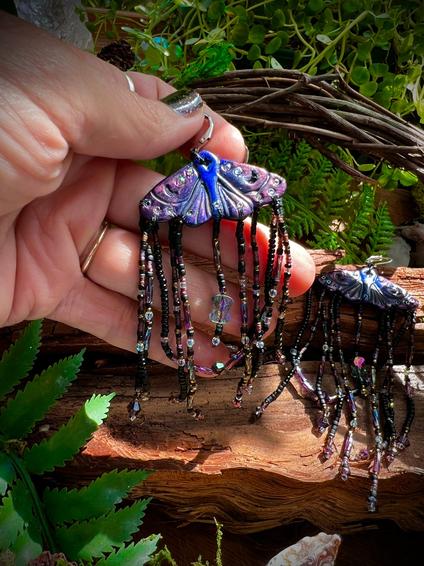 Lightweight polymer clay moth earrings with stainless steel hoops shown in natural forest light