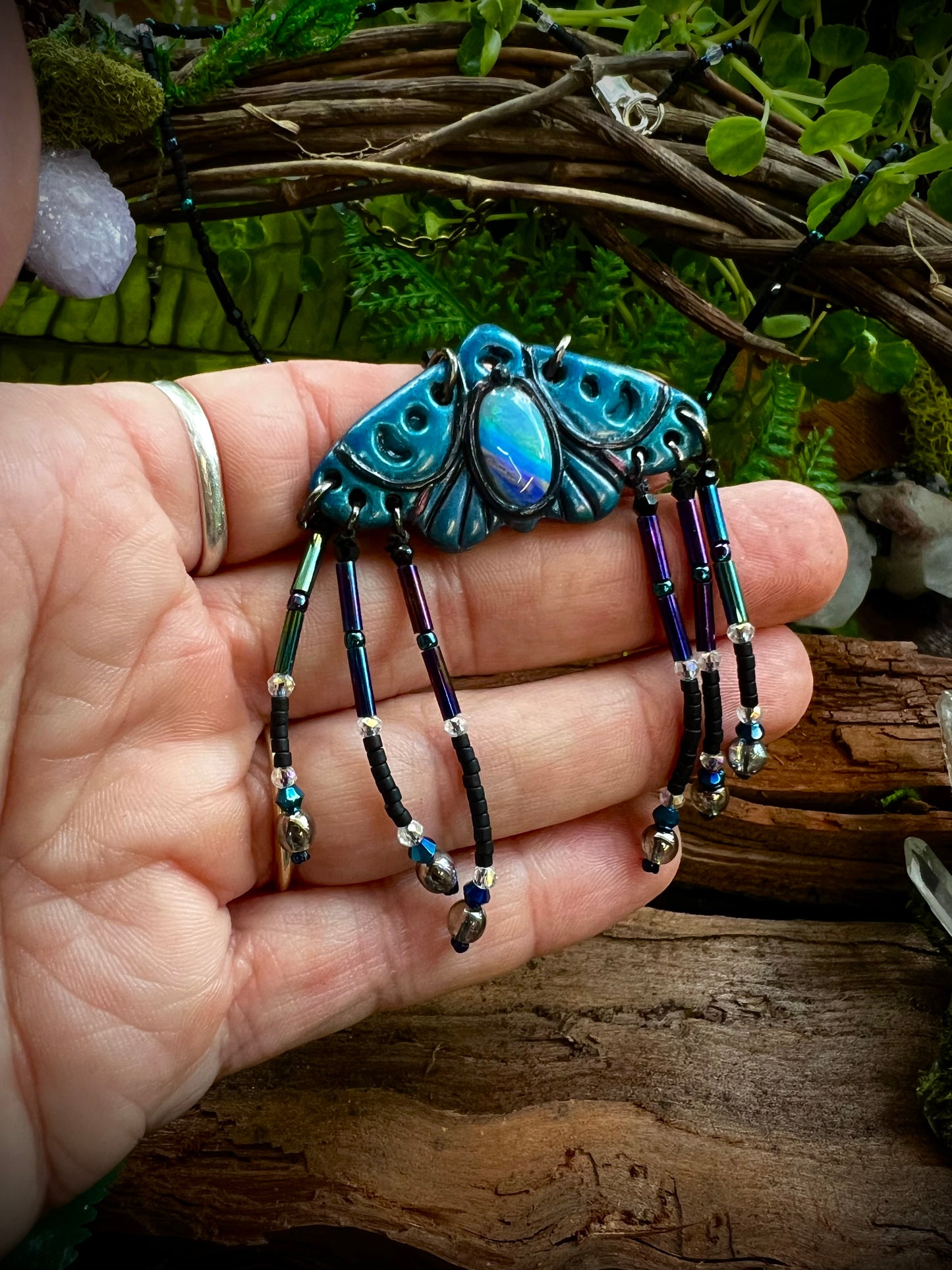 Opal moth necklace displayed on wood with crystal and greenery accents