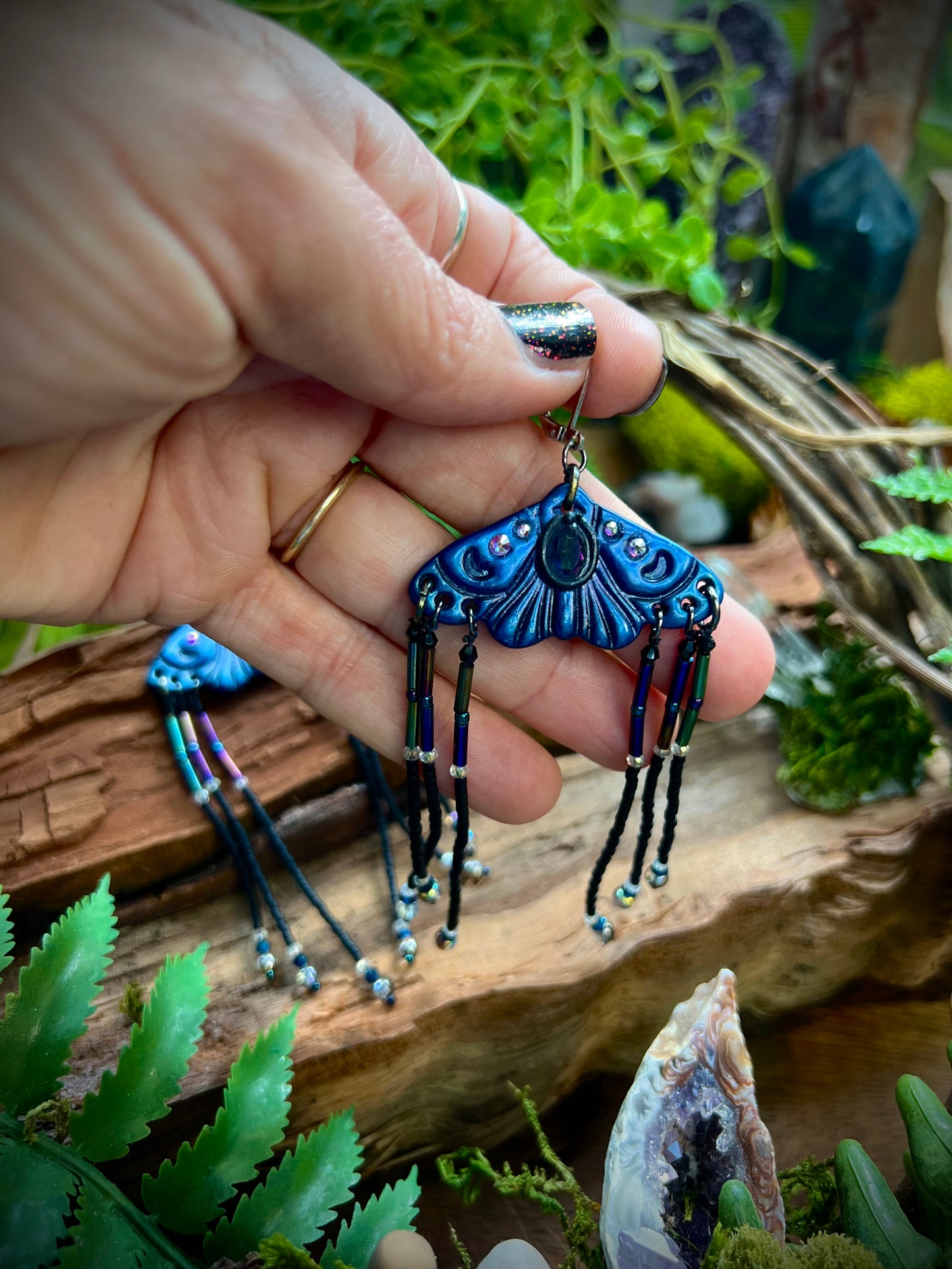 Seed bead fringe moth earrings displayed with natural quartz and moss accents