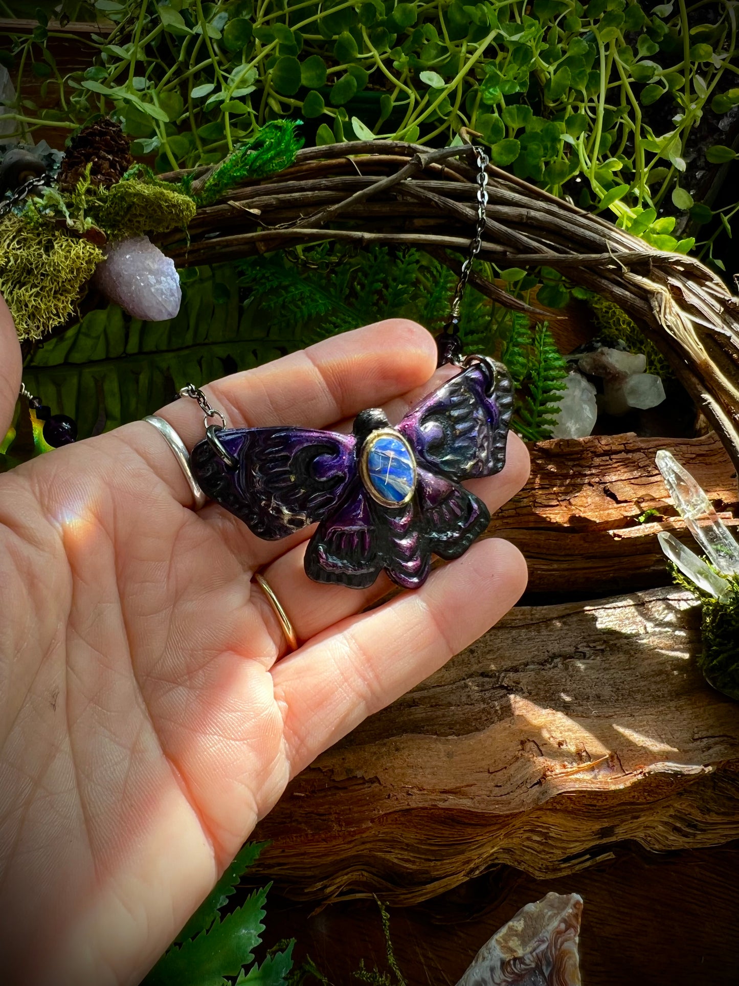 Spiritual moth necklace with protective gemstones styled with forest moss
