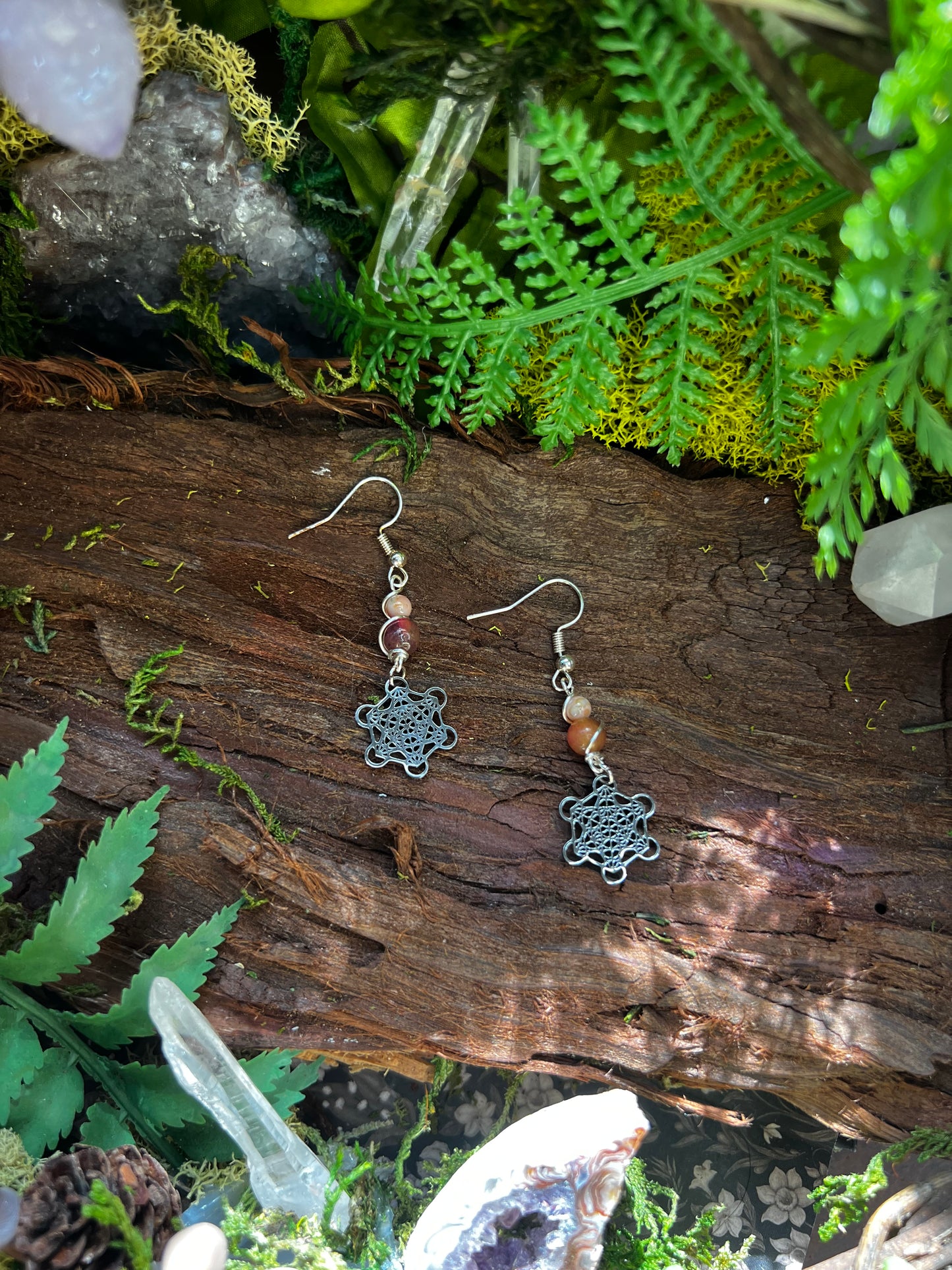 Pink jade Metatron earrings with sacred geometry charms resting on moss and wood