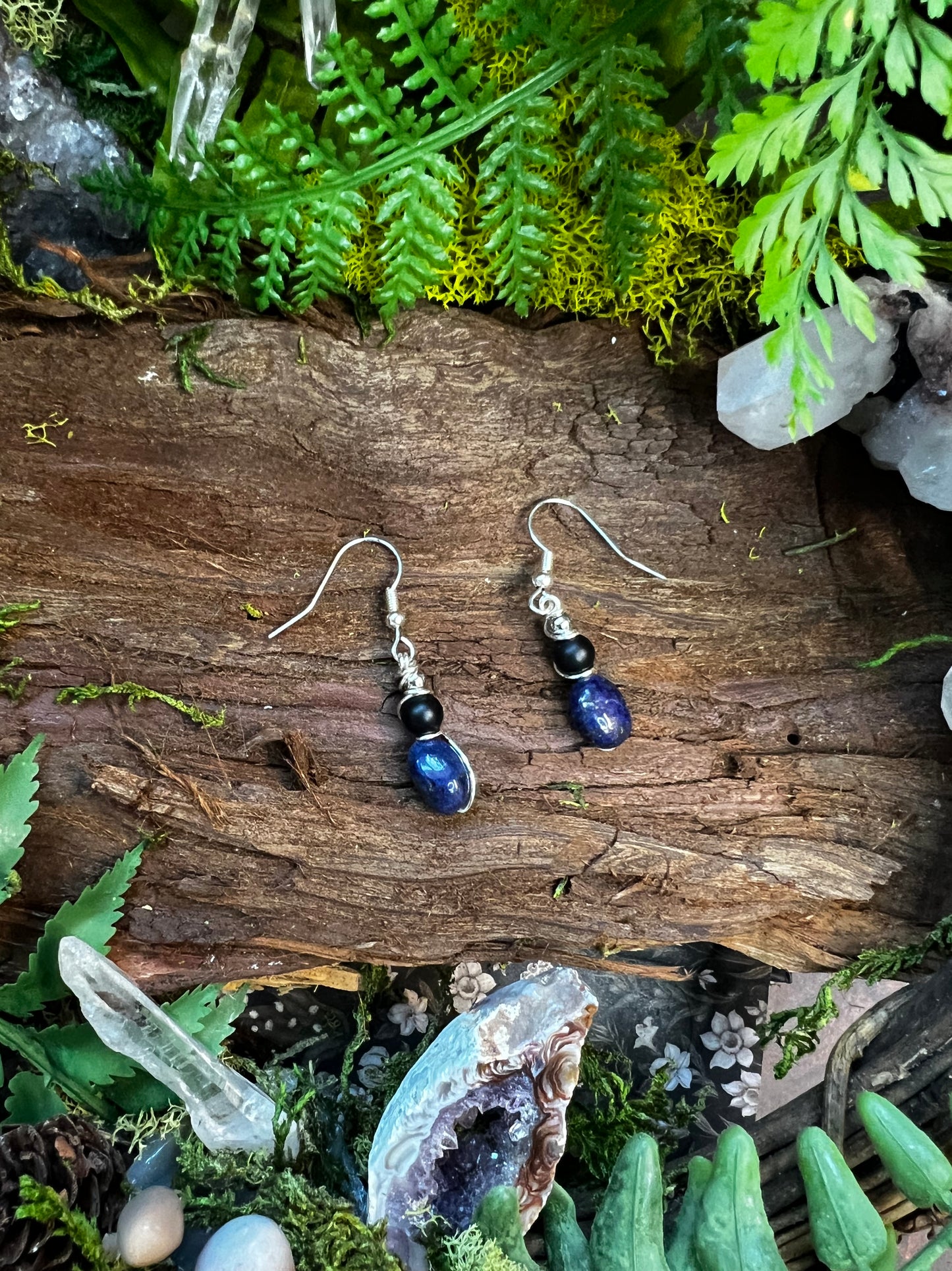 Lapis and onyx drop earrings resting on moss and wood with crystals