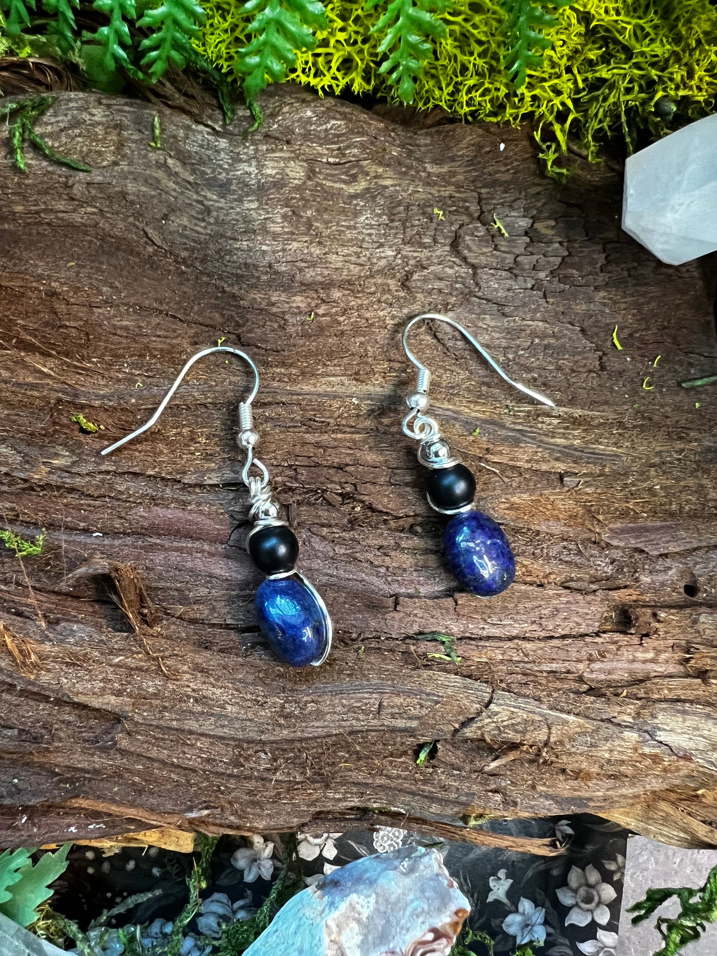 Black and deep blue crystal earrings styled on a rustic forest backdrop