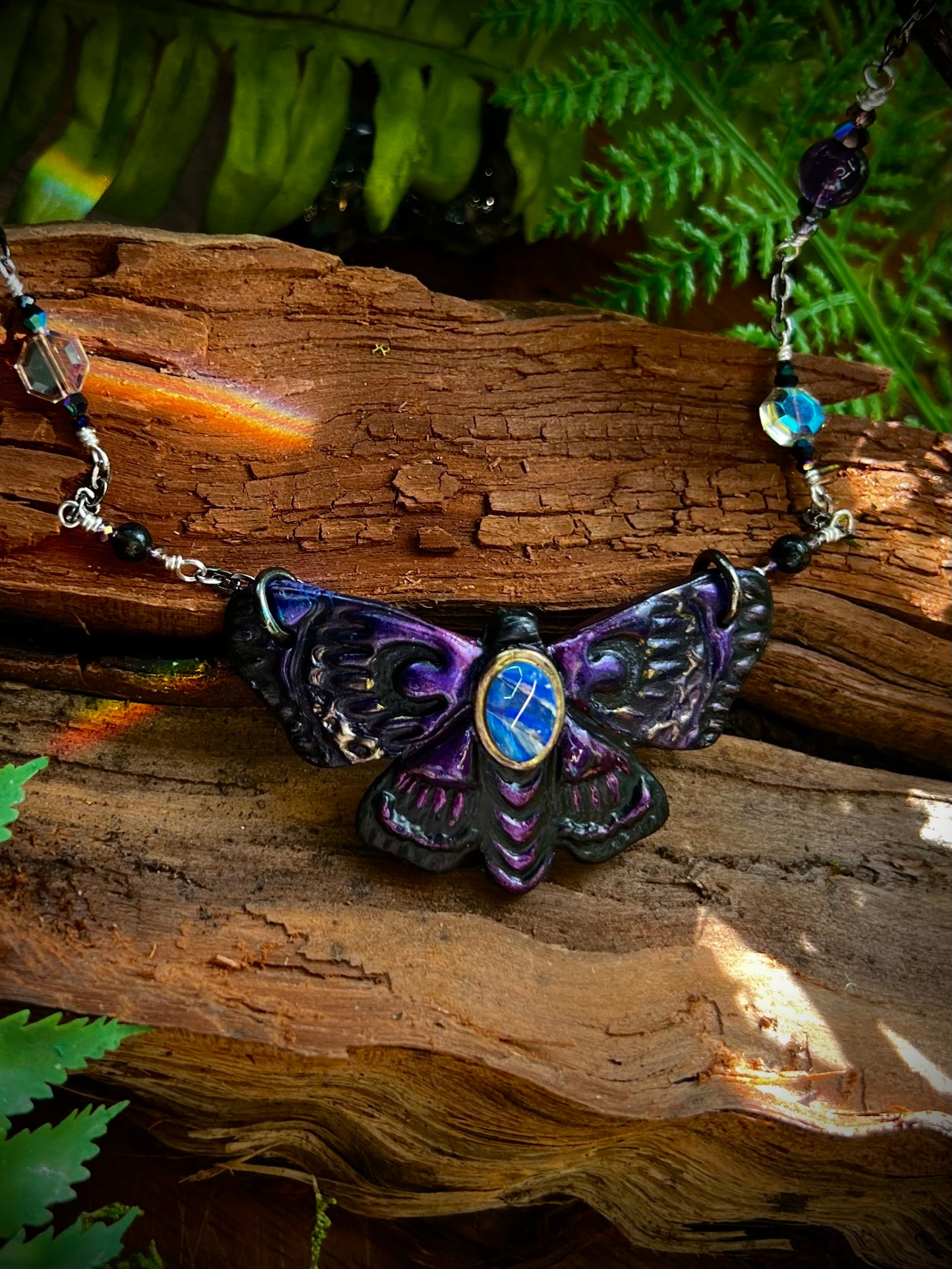 Close-up of opal moth pendant with shimmering violet and midnight wing details