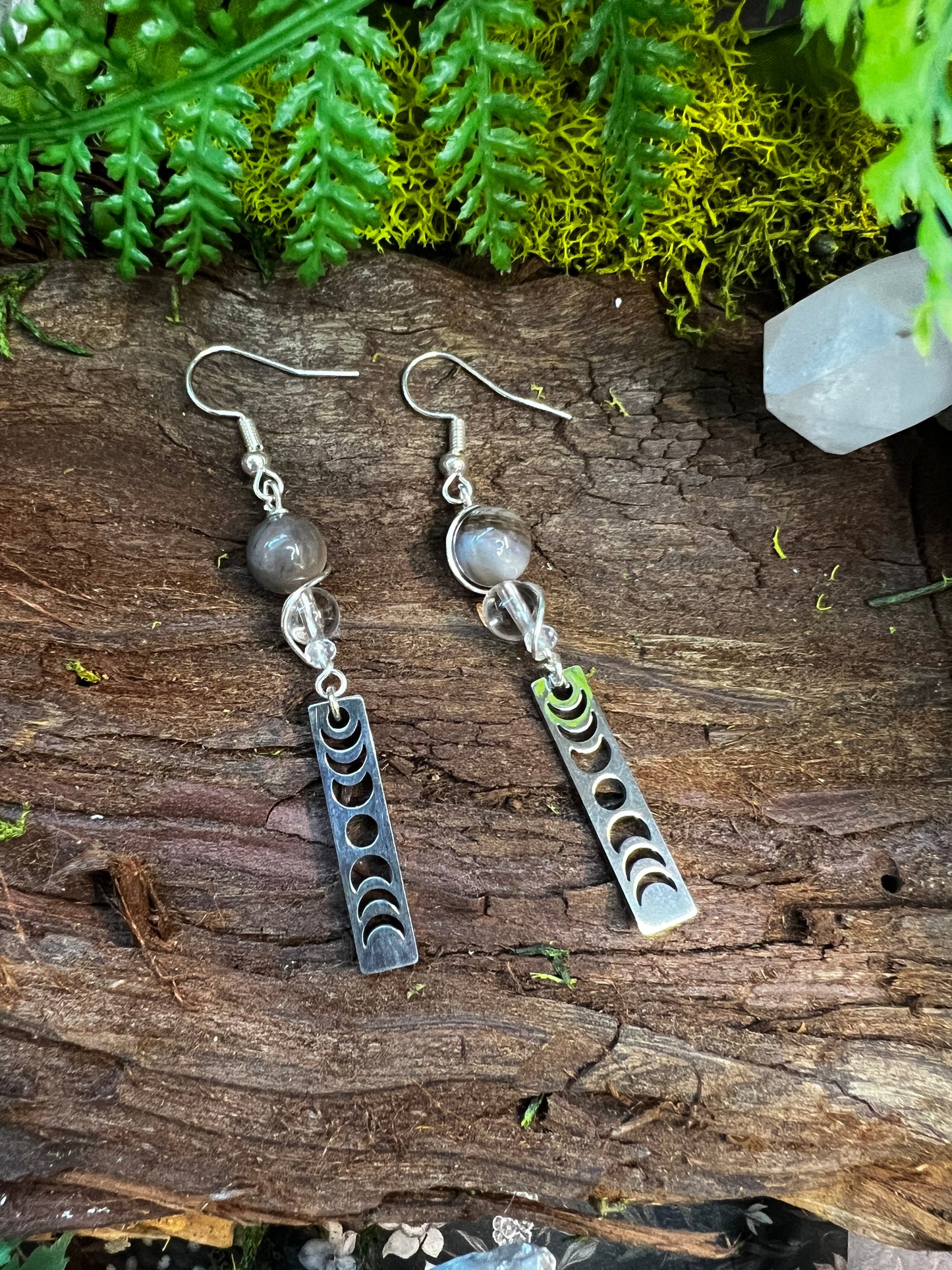 Petrified wood and clear quartz lunar phase earrings resting on mossy wood