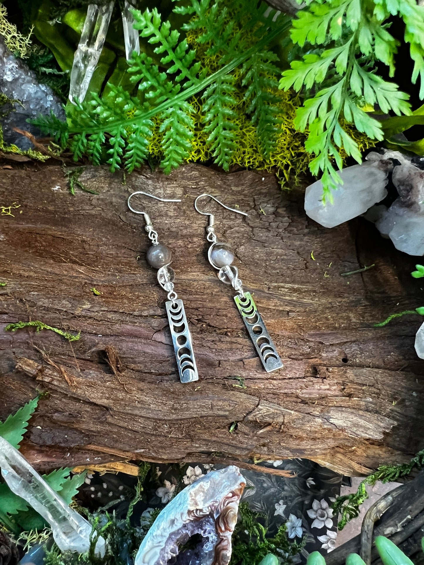 Earthy crystal earrings with moon phases styled on a forest-inspired background