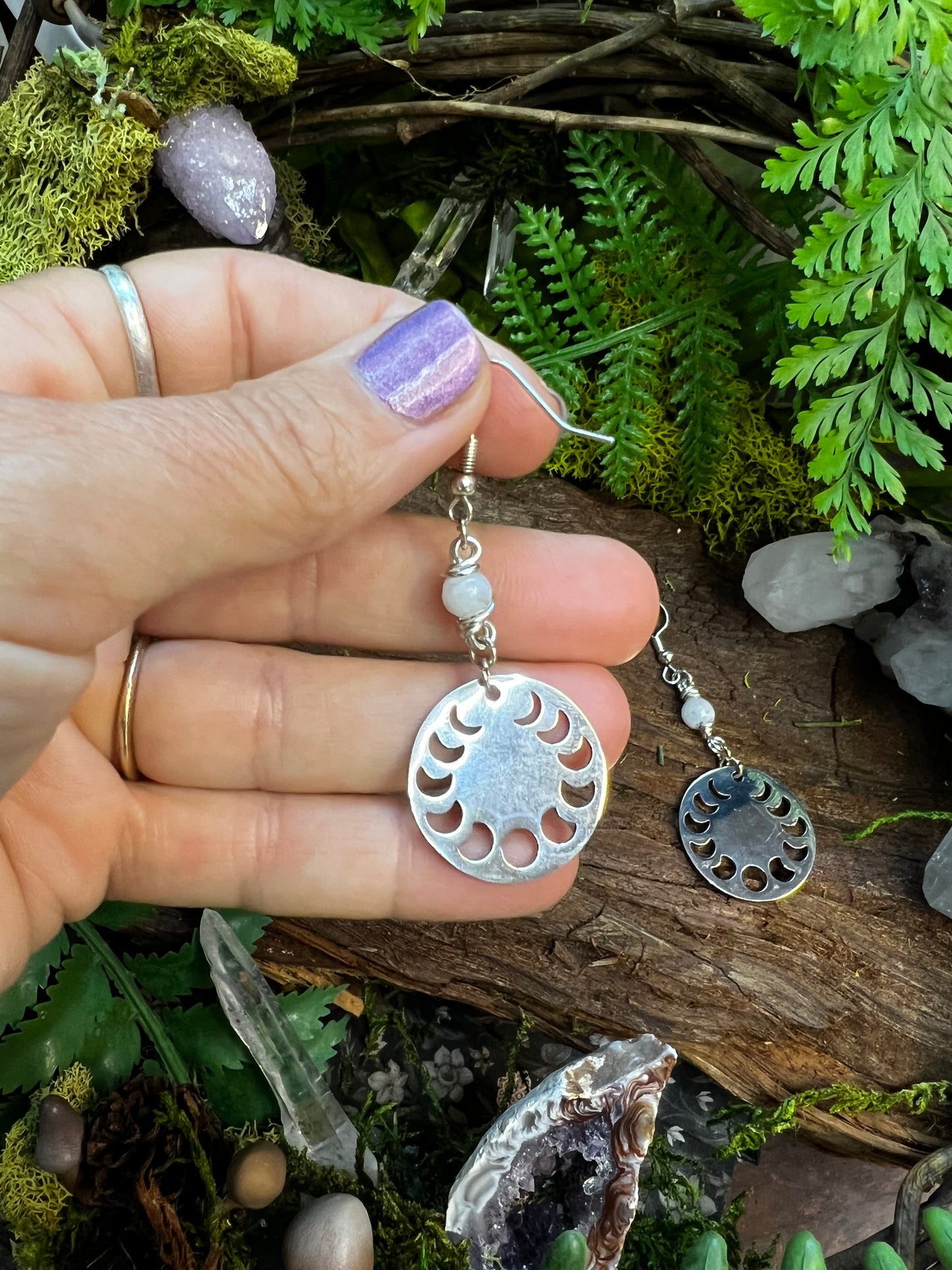 Mystical lunar earrings featuring moonstone and moon phases surrounded by greenery