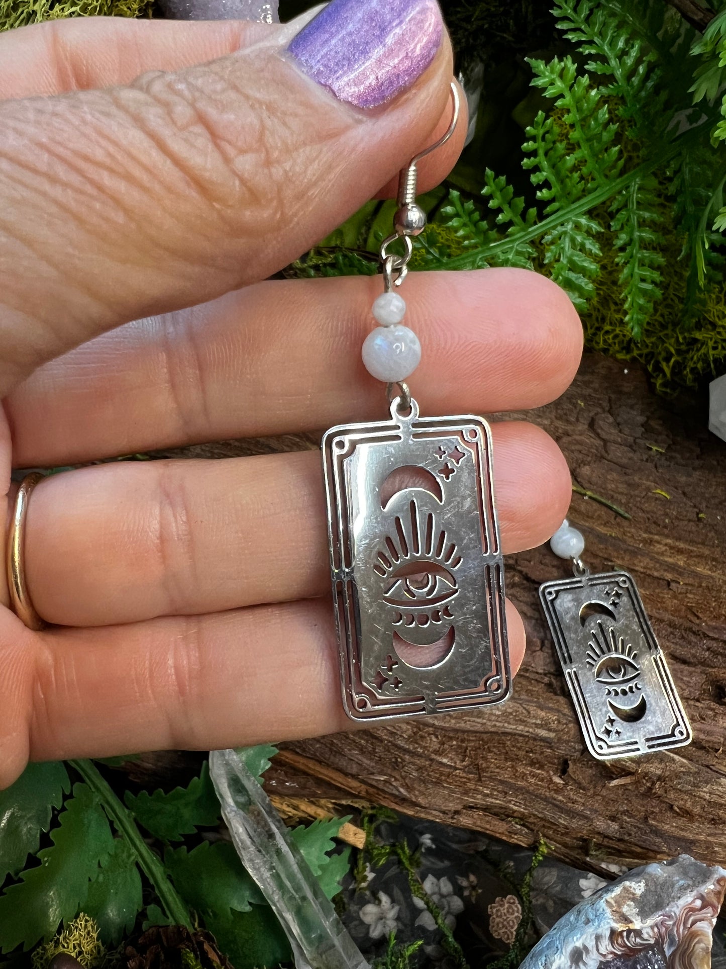 Mystical moonstone earrings featuring tarot-inspired charms surrounded by greenery