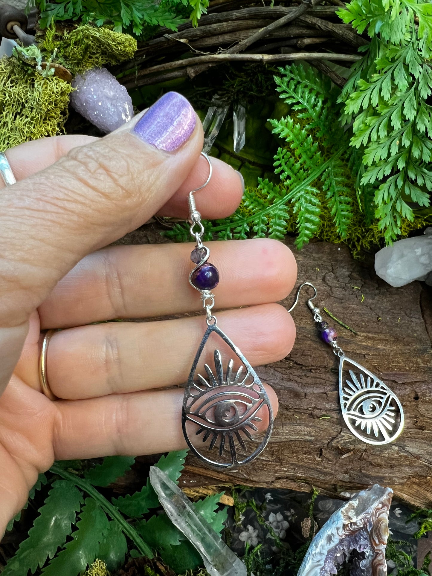 Protective crystal earrings with all-seeing eye charms on rustic forest backdrop
