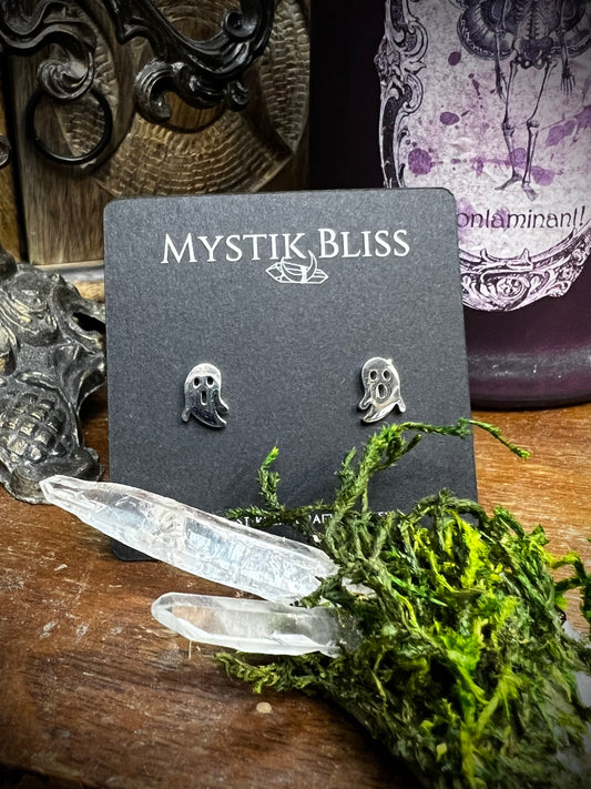 Silver ghost-shaped earrings on a 'Mystik Bliss' card with crystals and moss in the foreground.