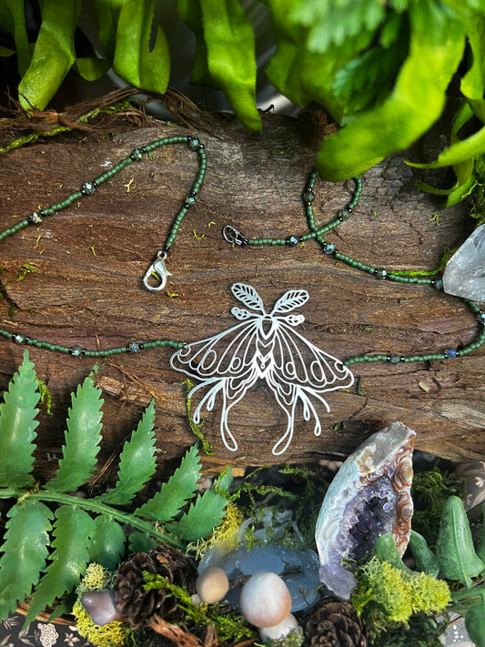 Close-up of hand holding necklace, highlighting subtle sparkle of green beads and silver moth charm
