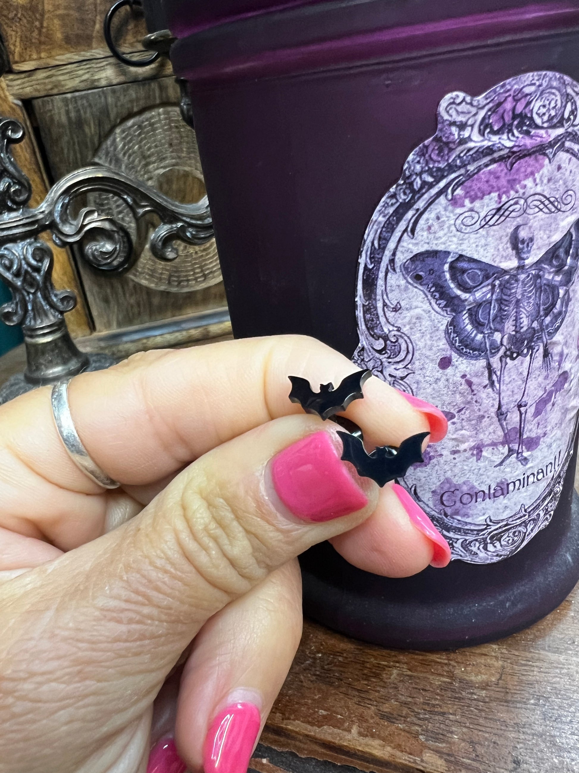 Hand holding a black bat-shaped earring with a decorative book in the background