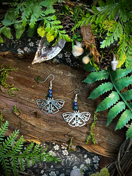 Silver moth earrings with chrysocolla and lapis lazuli displayed on a forest-themed altar.