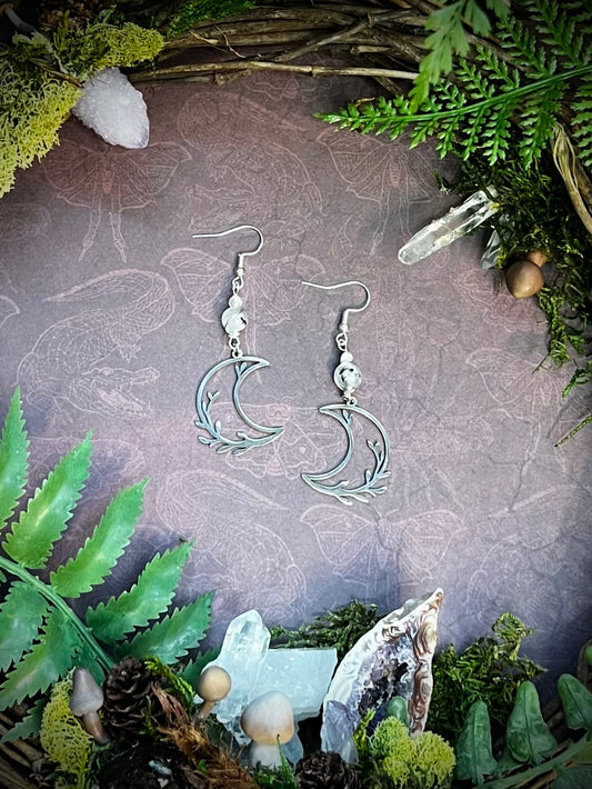 Rainbow moonstone earrings with crescent moon charms and forest altar setting