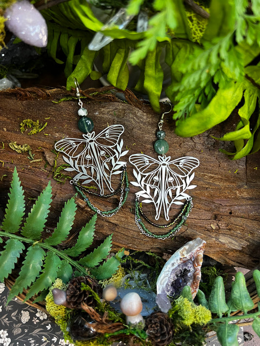 Moss agate moon moth earrings with green beads styled on mossy wood