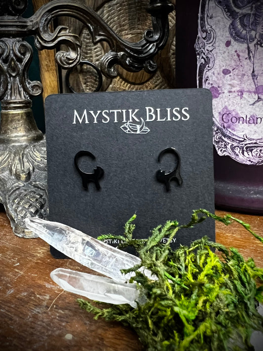 Mystik Bliss black cat earrings on a display card with crystals and moss on a wooden surface