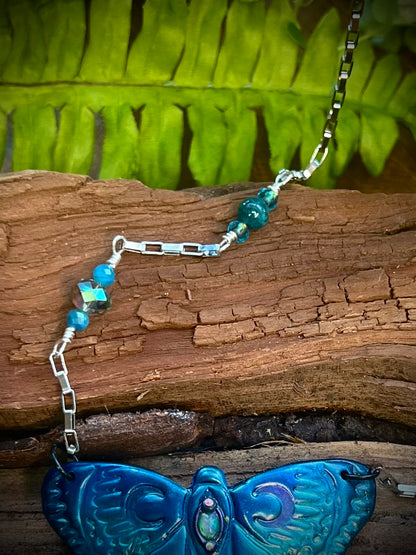Mystical moth pendant displayed on wood with ferns and crystals