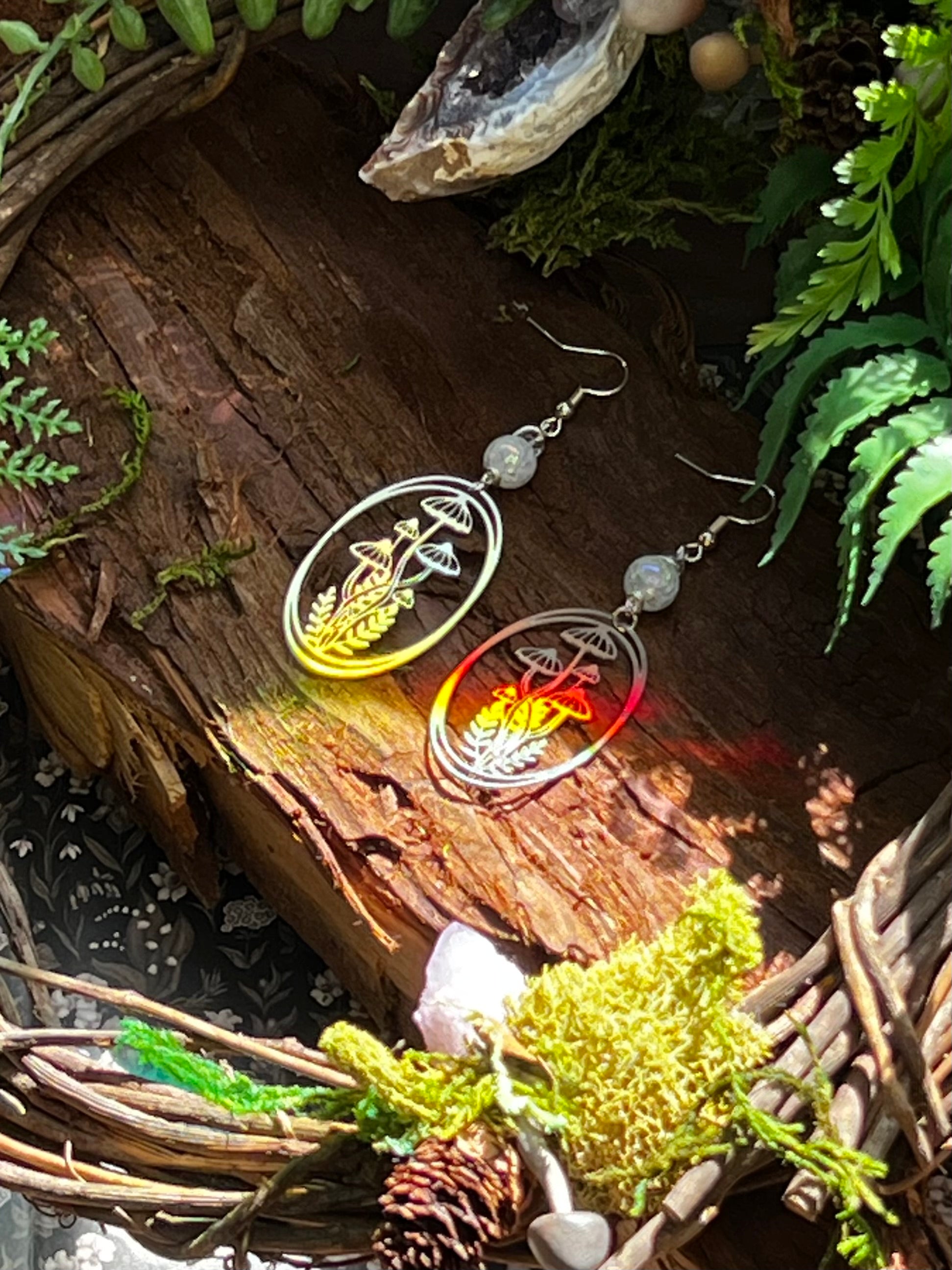 Forest-inspired earrings with aura crackle quartz and stainless steel mushroom charms displayed on natural wood