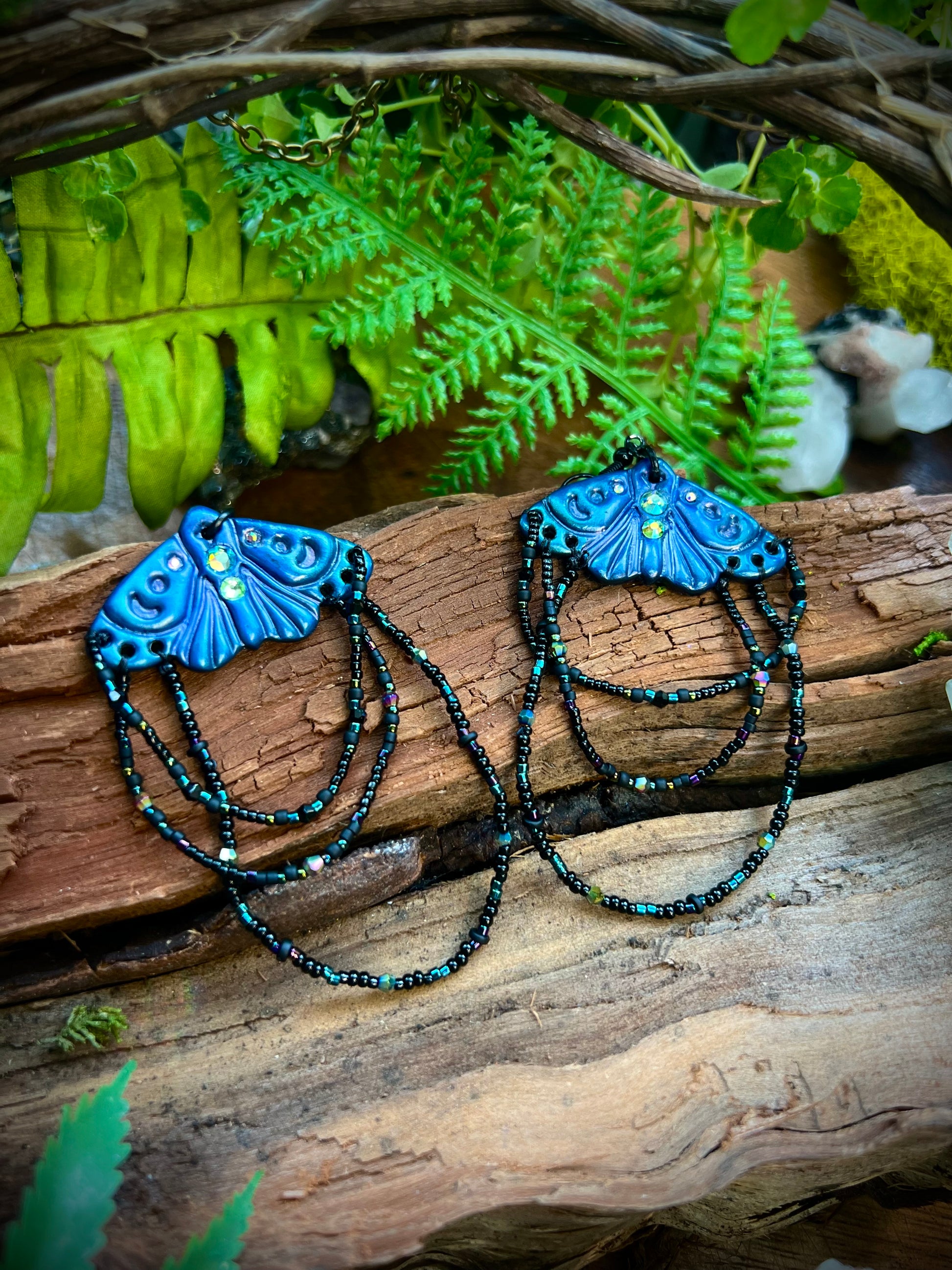 Mystical moth earrings displayed against wood and greenery