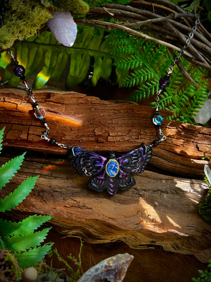 Mystical moth necklace with gemstone beads displayed against rustic wood