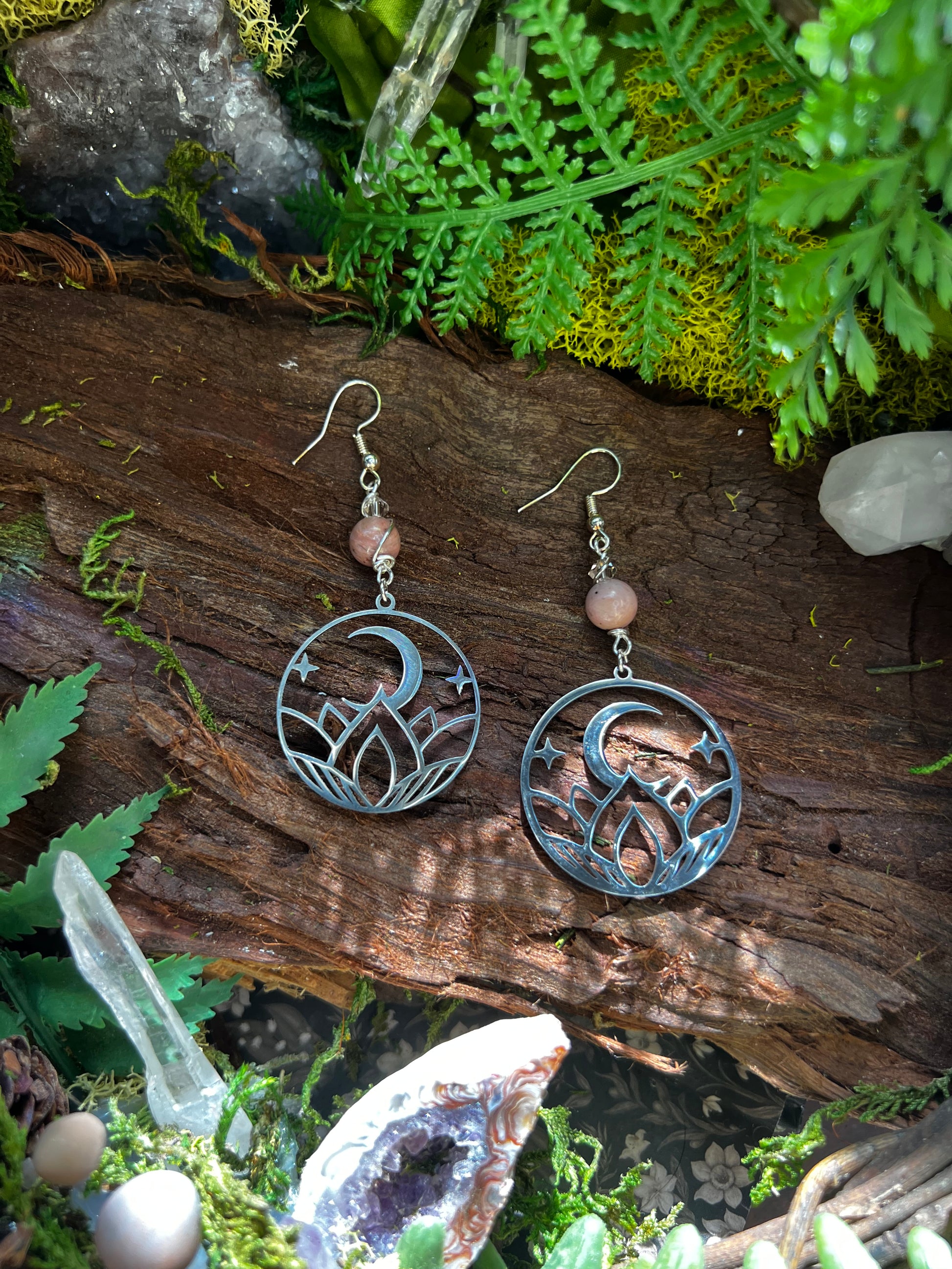 Rhodonite moon phase earrings with lotus and crescent moon charms on forest moss background