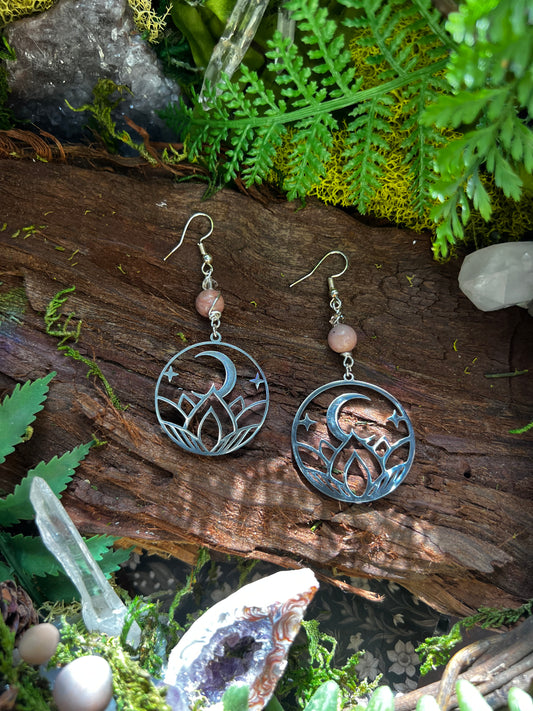 Rhodonite moon phase earrings with lotus and crescent moon charms on forest moss background
