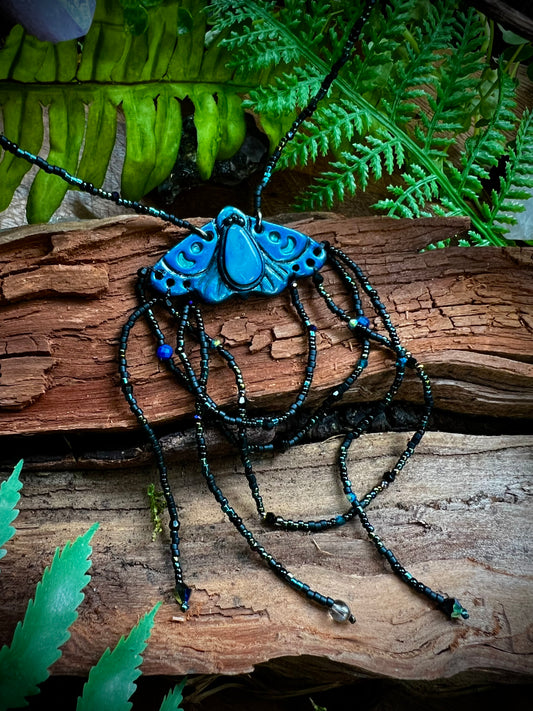 Woodland moth necklace styled among moss, quartz, and forest accents