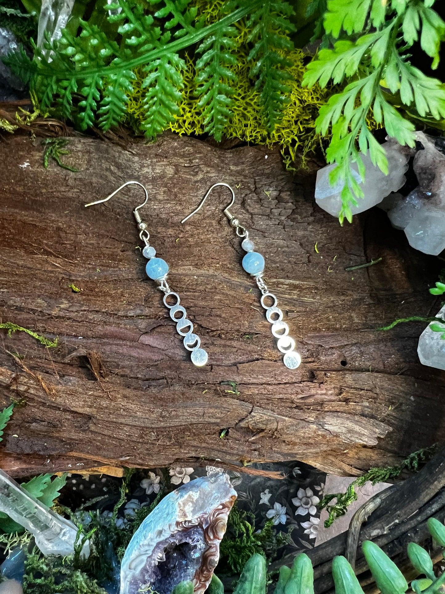 Calming crystal earrings with moon phase charms on natural forest backdrop