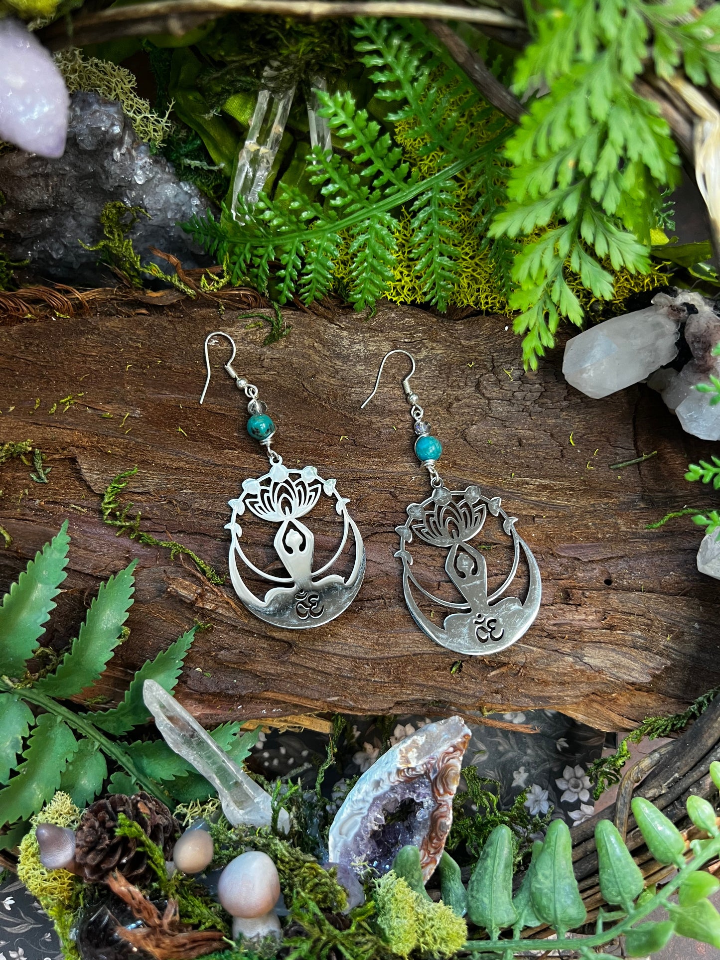 Calming crystal earrings with Om and lotus design resting on a natural forest backdrop