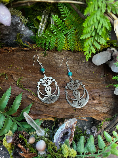 Calming crystal earrings with Om and lotus design resting on a natural forest backdrop