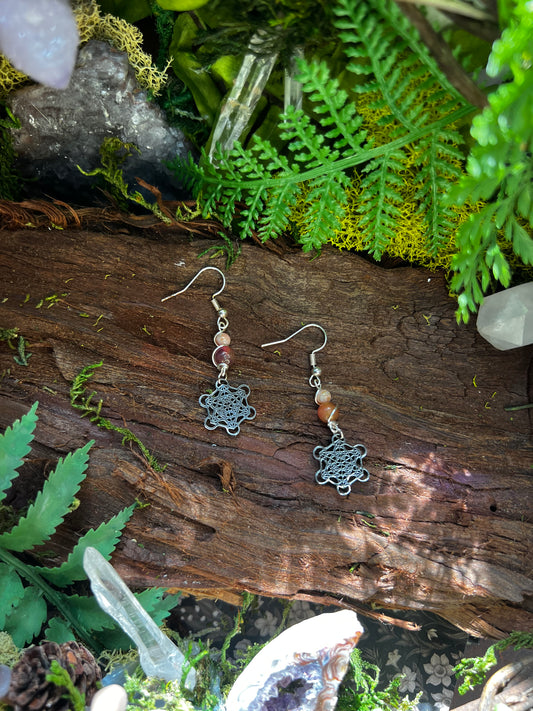 Pink jade Metatron earrings with sacred geometry charms resting on moss and wood