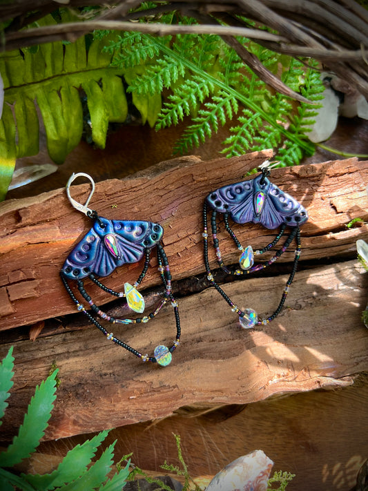 Handcrafted polymer clay moth earrings with iridescent crystal dangles in sunlight
