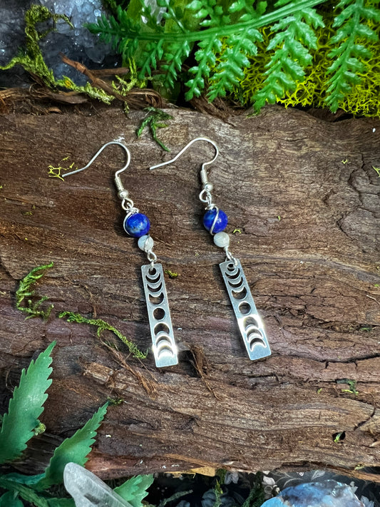 Lapis and moonstone lunar phase earrings styled on wood with moss and crystals