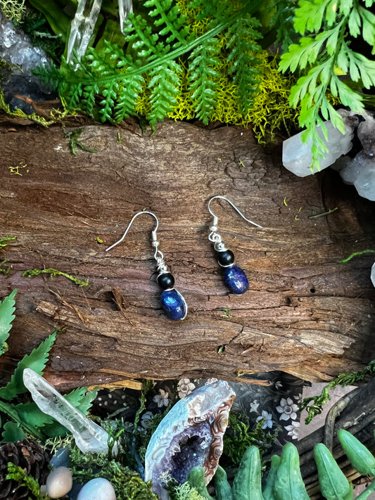 Lapis and onyx drop earrings resting on moss and wood with crystals