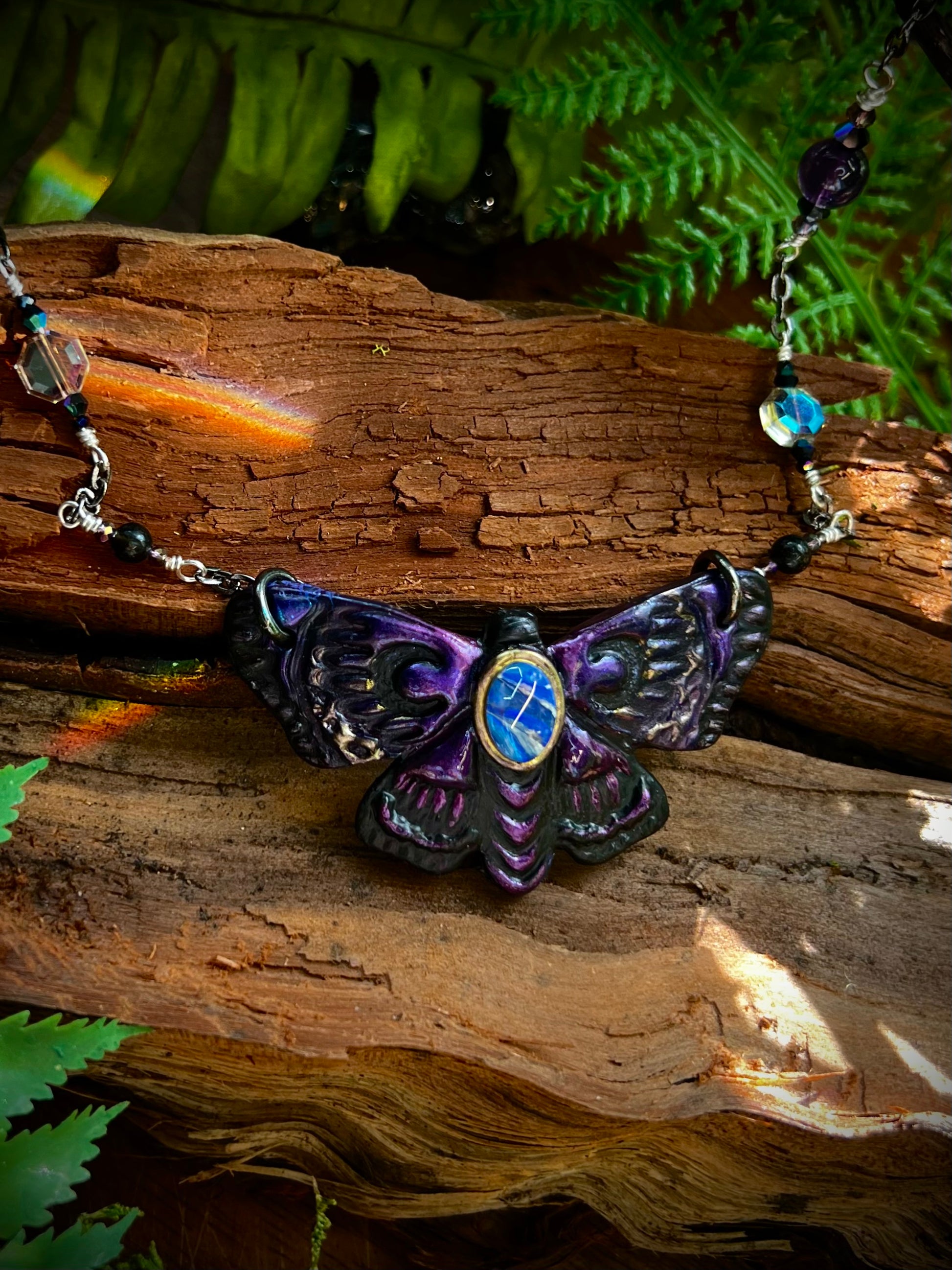 Close-up of opal moth pendant with shimmering violet and midnight wing details
