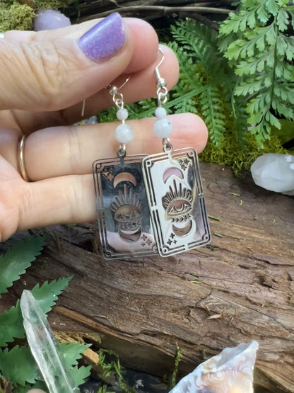 Intuitive jewelry with rainbow moonstone and tarot card symbols on wooden surface
