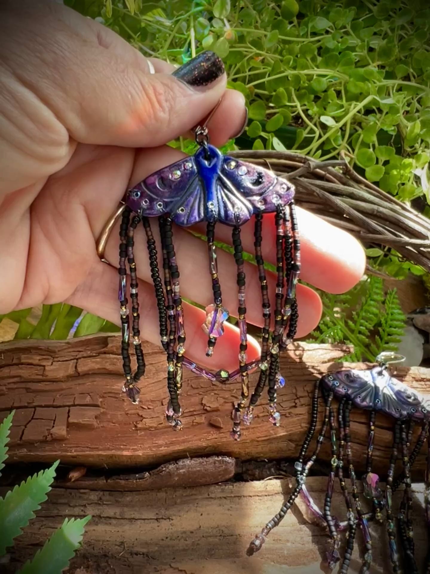 Close-up of iridescent beaded tassels shimmering in rainbow light on moth earrings
