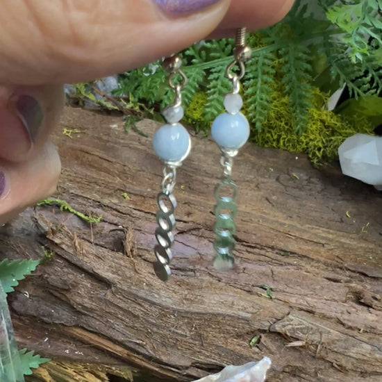 Serene aquamarine and moonstone earrings surrounded by greenery and crystal accents